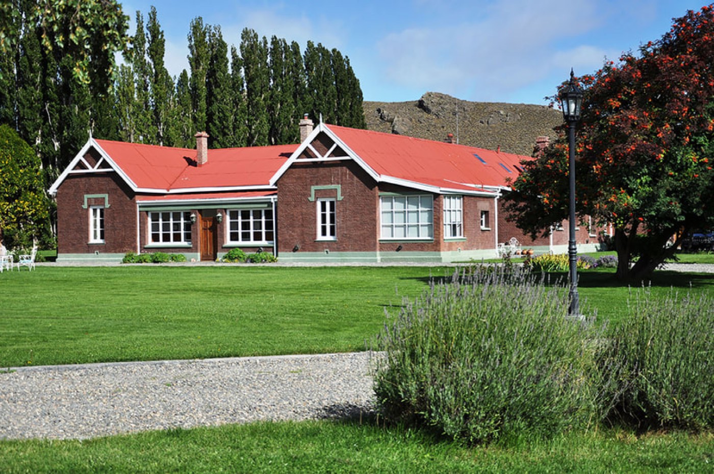 A red-roofed brick building framed by poplars, with a lamppost and lavender in the foreground
