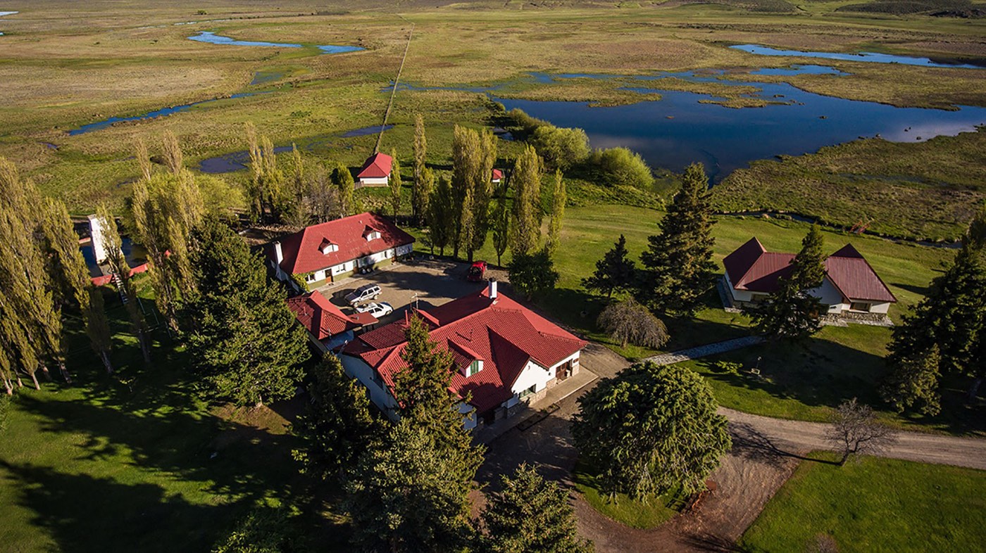 A closer aerial view of the lodge complex among poplars and pines, with a lagoon just behind the buildings