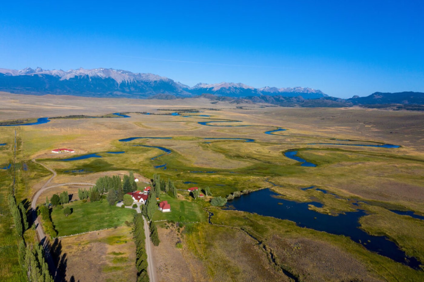 Golden marshland threaded with winding blue river channels, snow-capped mountains on the horizon