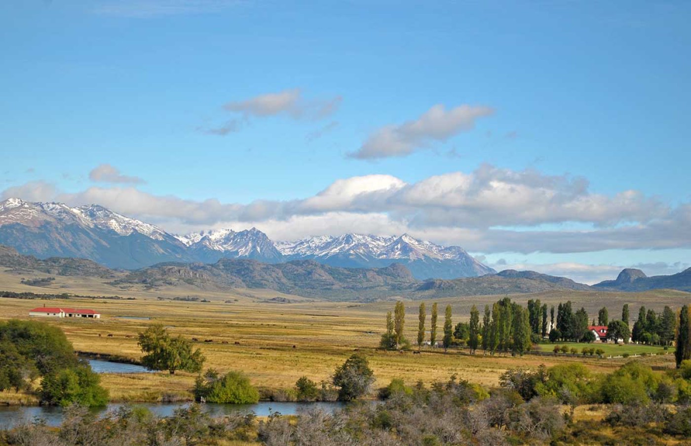 Grassland with a meandering river beneath a mountain range dusted with snow