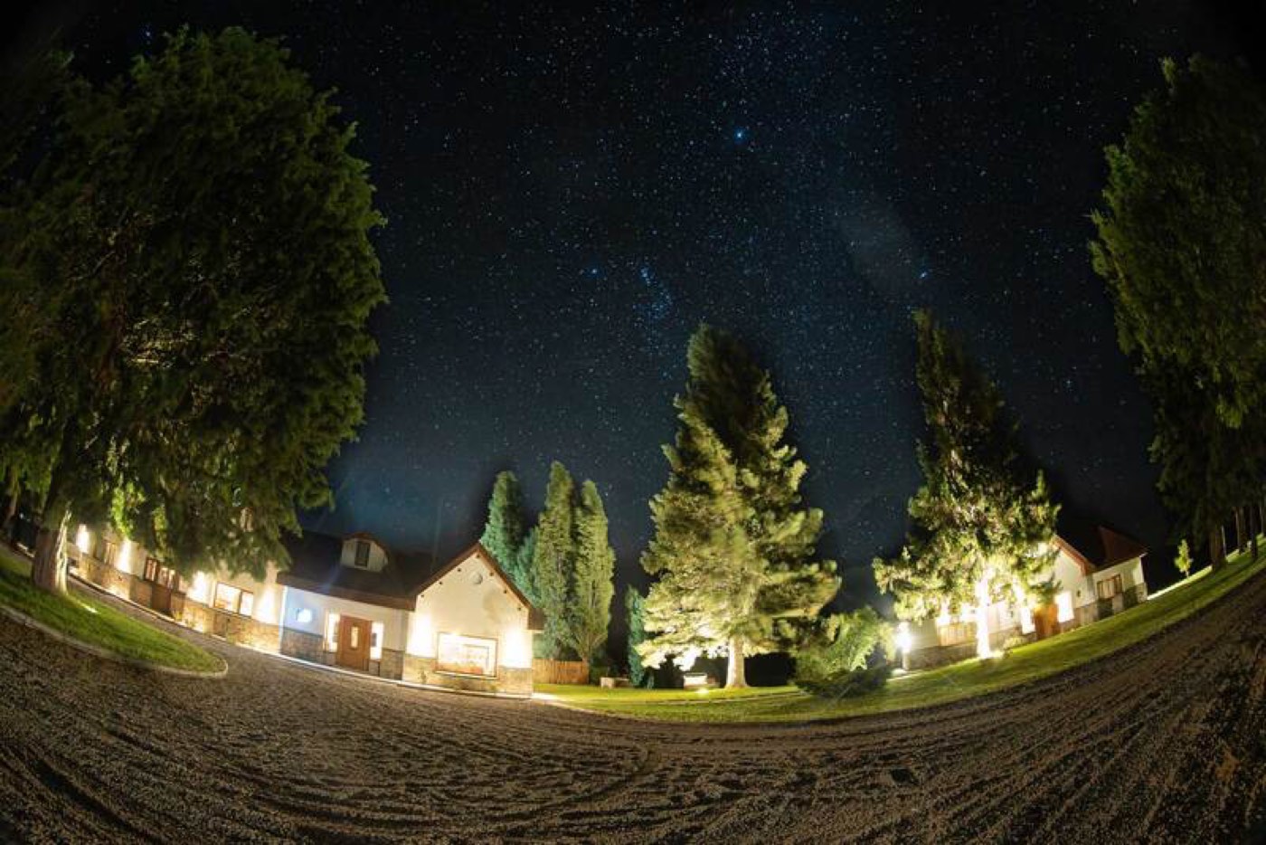 A fisheye view of a dense star field over the lodge's illuminated buildings at night