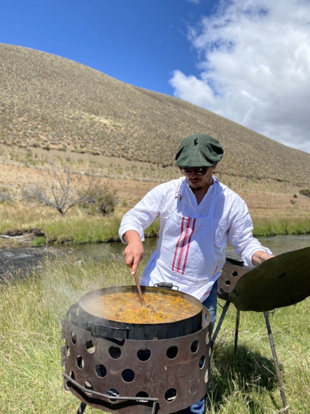 The lodge's chef, in whites and a beret, stirring a large pot of stew over an open fire