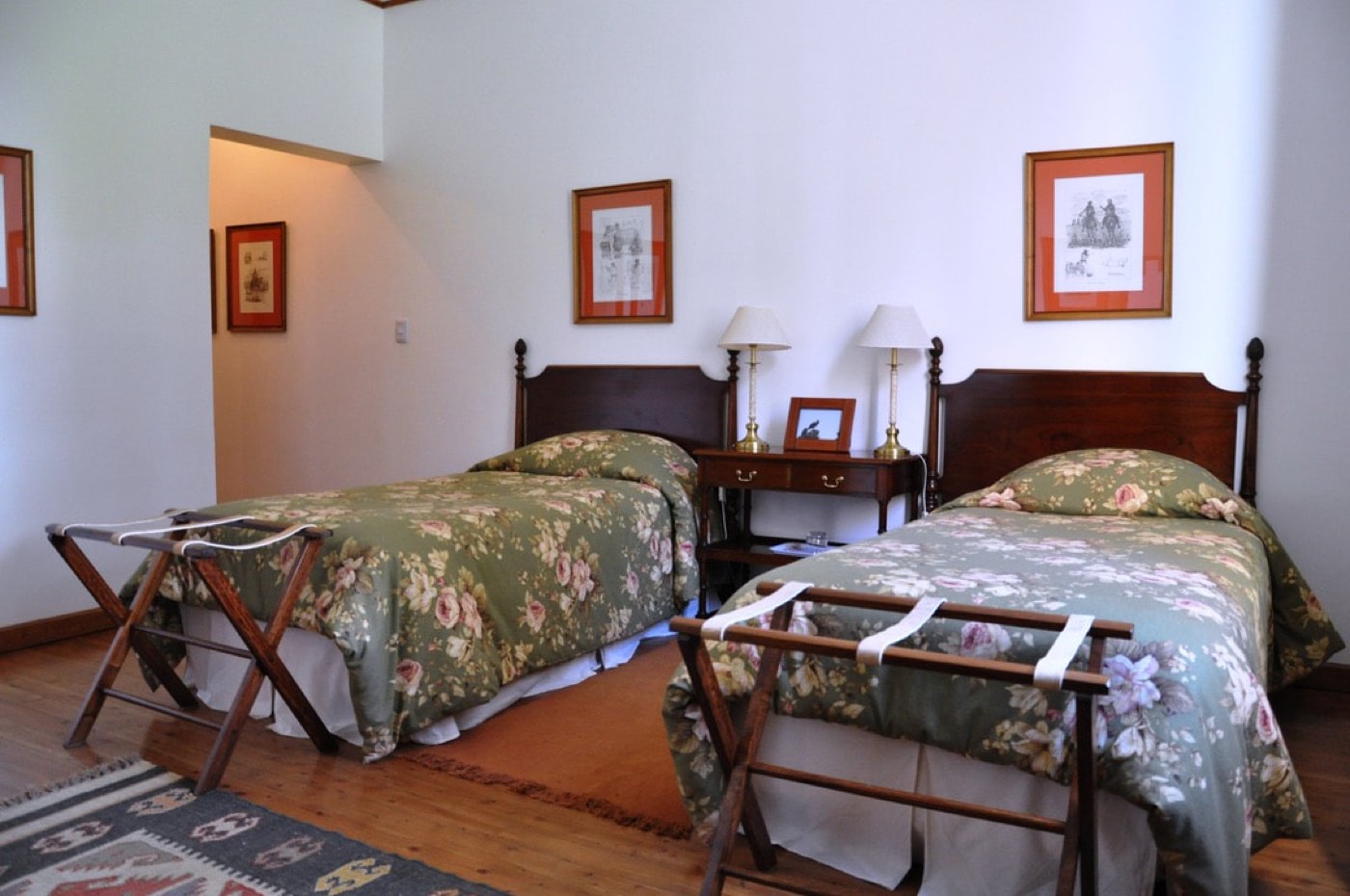 A twin room with sage-green floral bedspreads, vintage equestrian prints, and a kilim-style rug