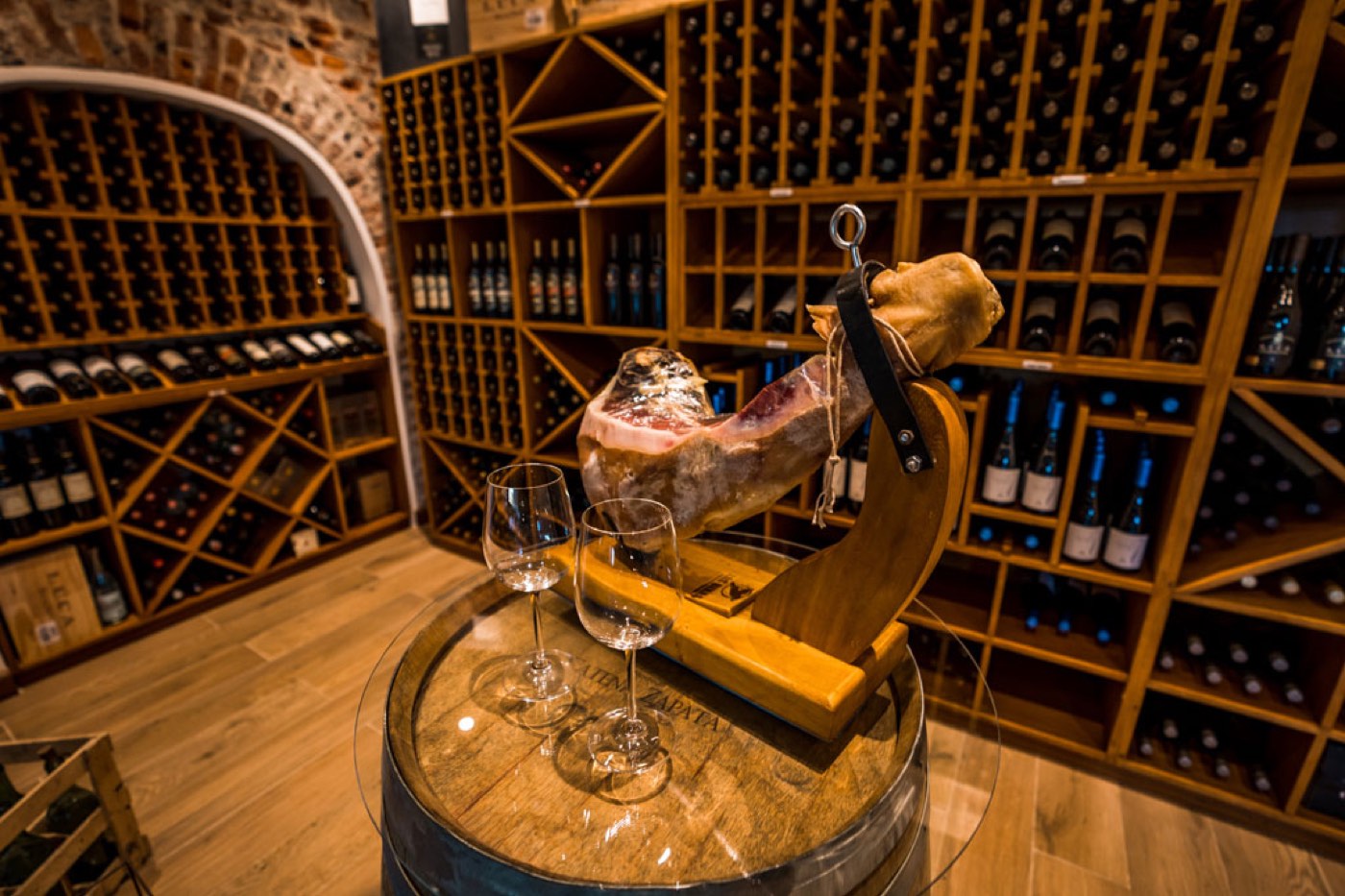 A cured leg of ham on a carving stand beside two glasses of wine in the lodge's wine cellar