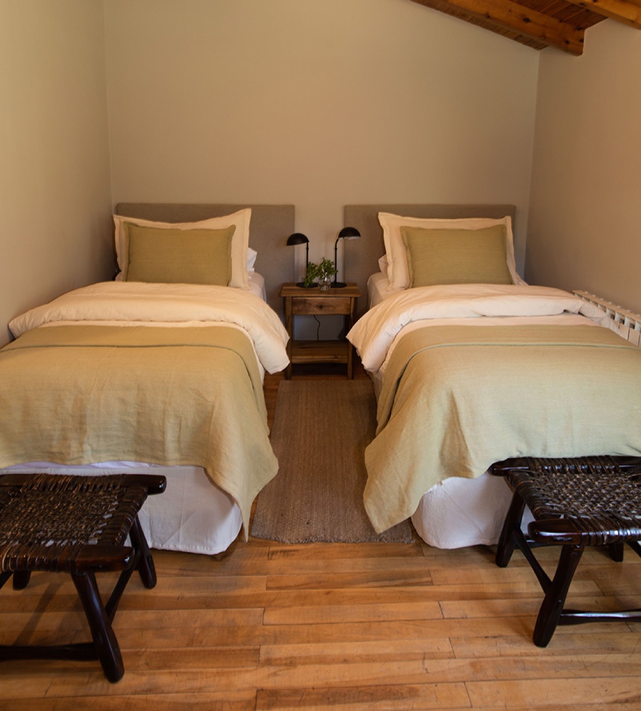 A twin room tucked under a sloped wood-beam ceiling, two single beds flanking a shared nightstand