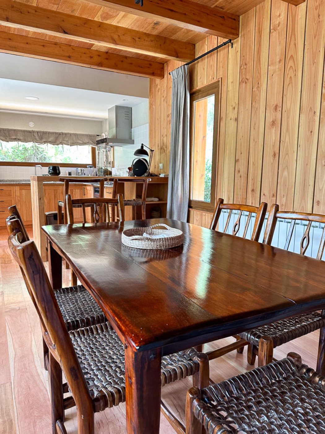 A wood-paneled dining room with a long table, opening onto the lodge's kitchen