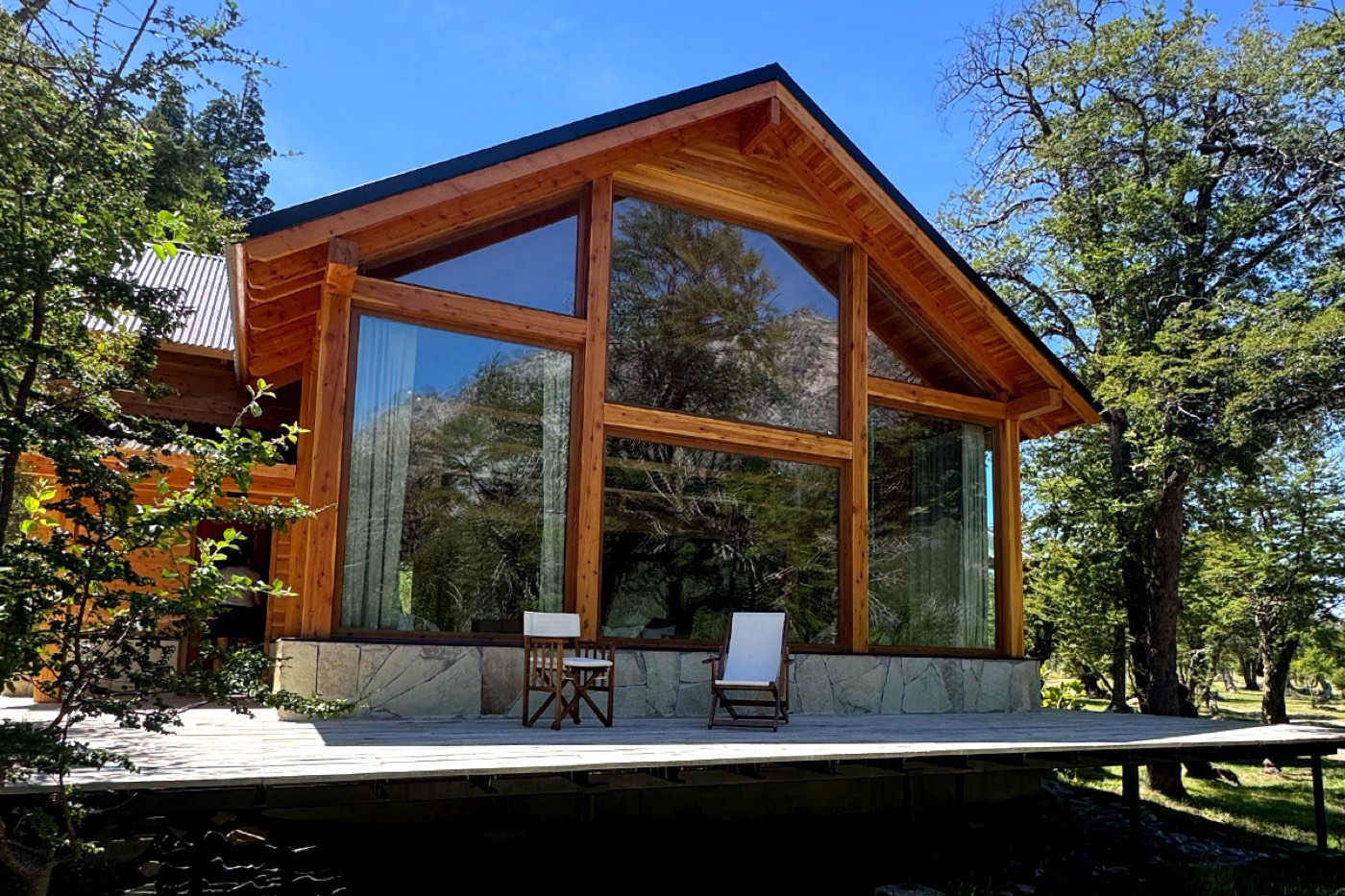 The exterior of a glass-walled guest building with a peaked timber roof, framed by trees