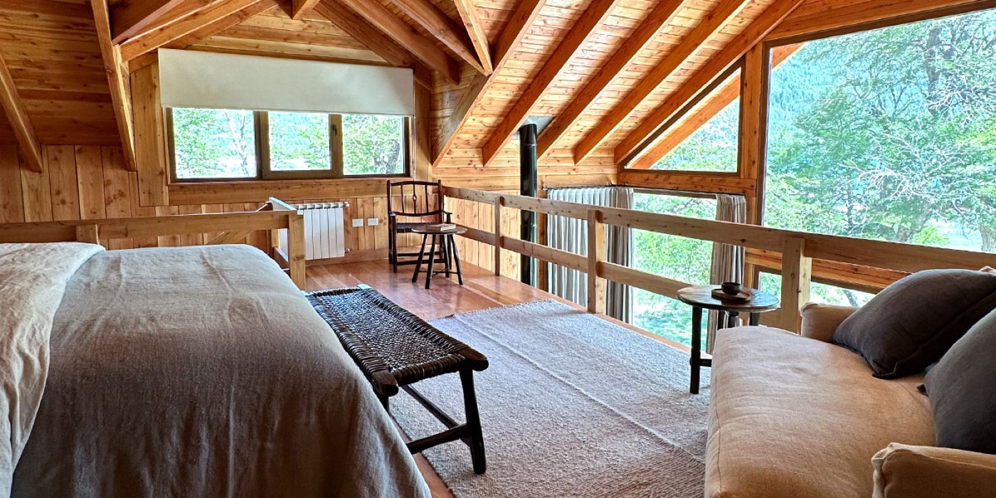 An open loft sleeping area under a wood-beam ceiling, overlooking the floor below through a timber railing