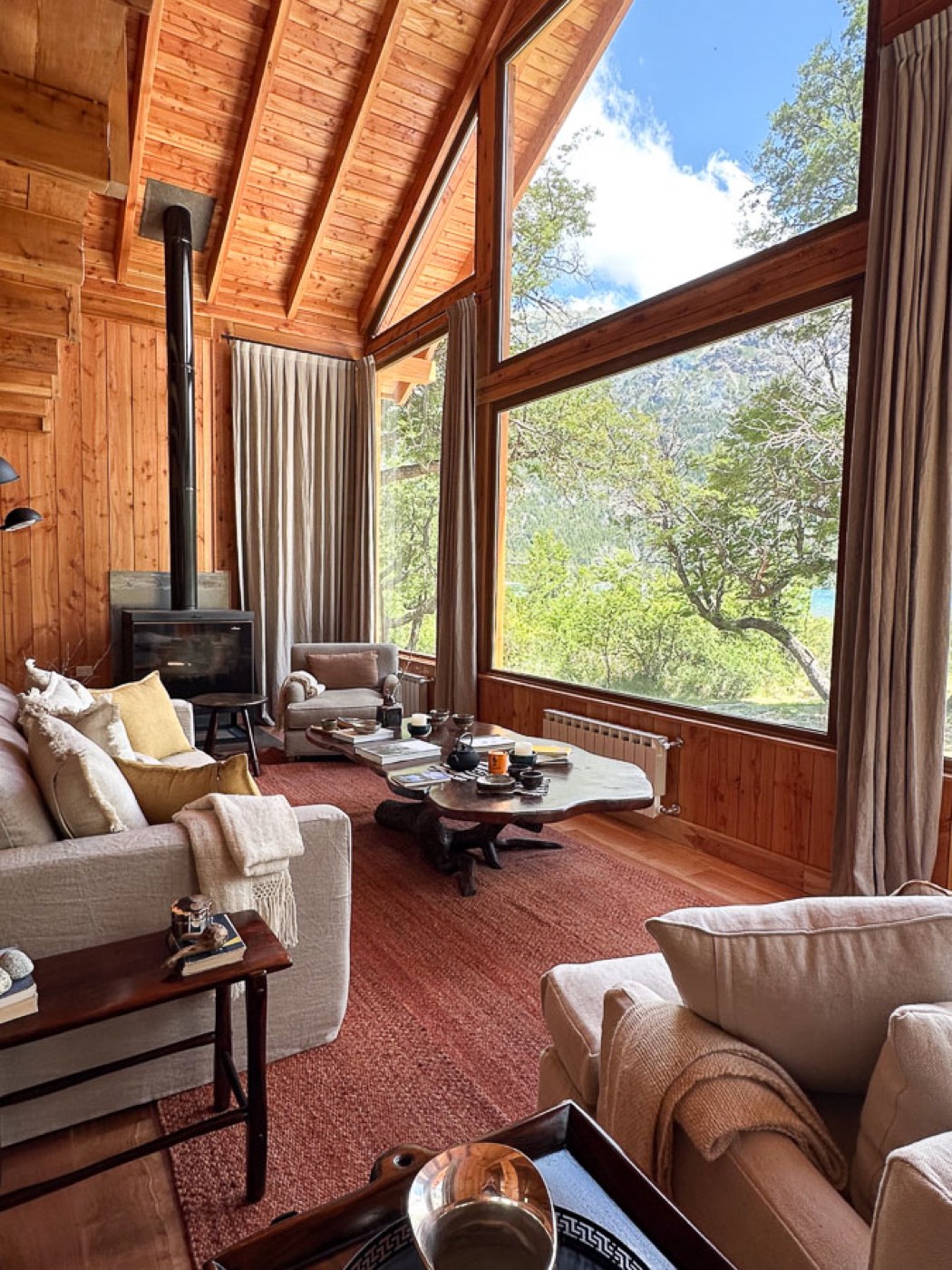 A living room warmed by a wood-burning stove, floor-to-ceiling windows facing the forested mountainside