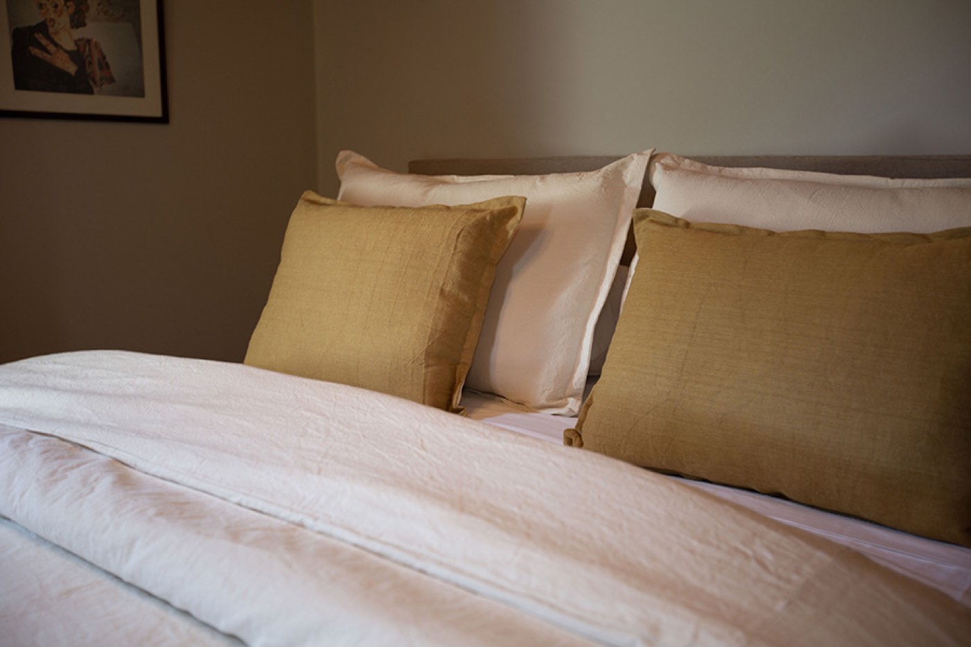 A close view of a made bed with white linens and olive-green throw pillows