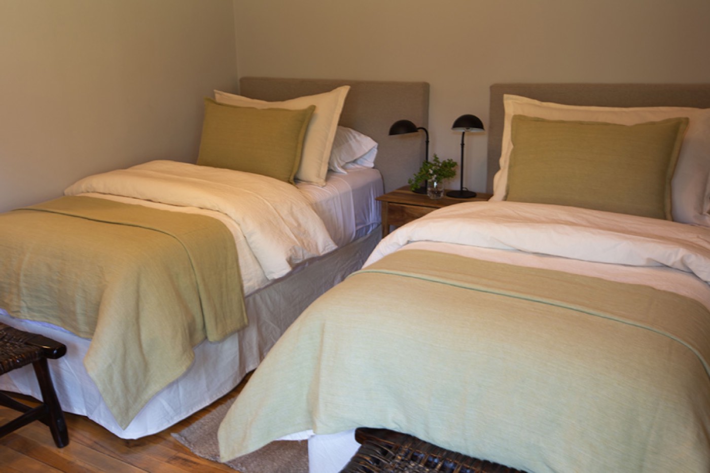 A twin room with two single beds in sage-green coverlets, sharing a nightstand between them