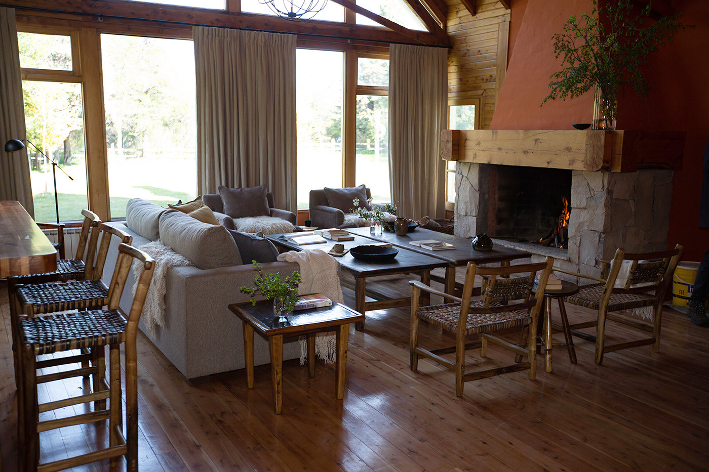 A great room with a vaulted wood-beam ceiling, a lit stone fireplace, and sectional seating facing the lawn