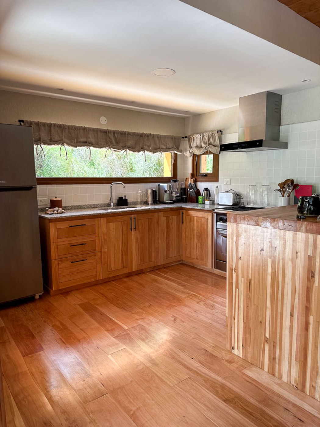 A modern kitchen with wood cabinetry, a butcher-block island, and a garden view