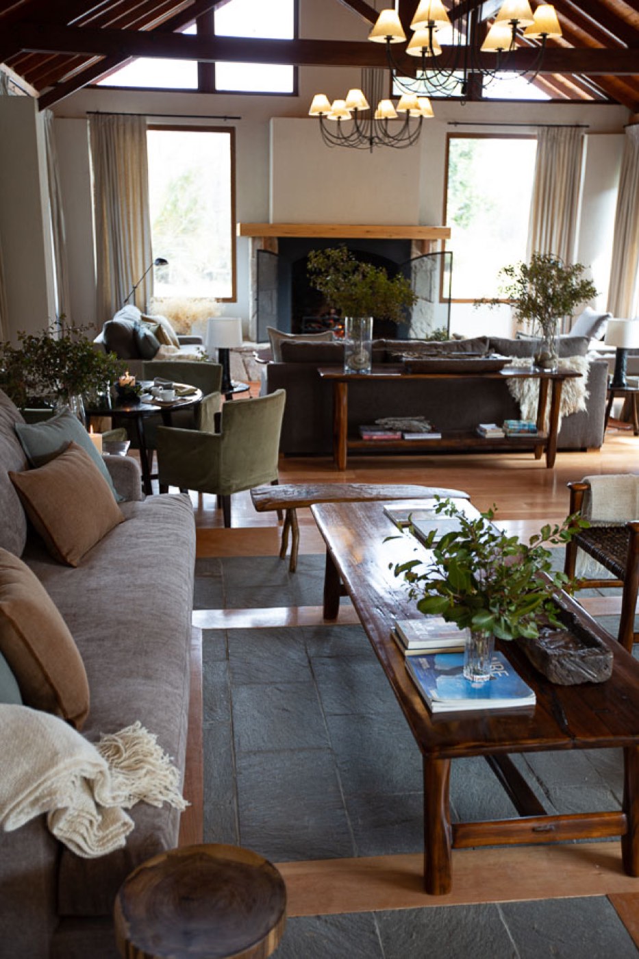 A great room with a wrought-iron chandelier, a lit stone fireplace, and sofas arranged for conversation
