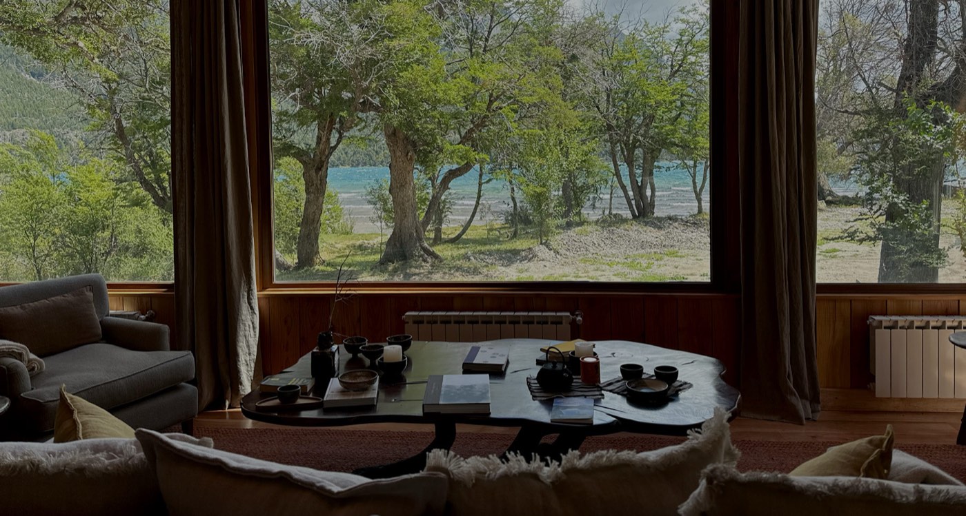 A living room with a round coffee table set for tea, floor-to-ceiling windows onto the lakeshore
