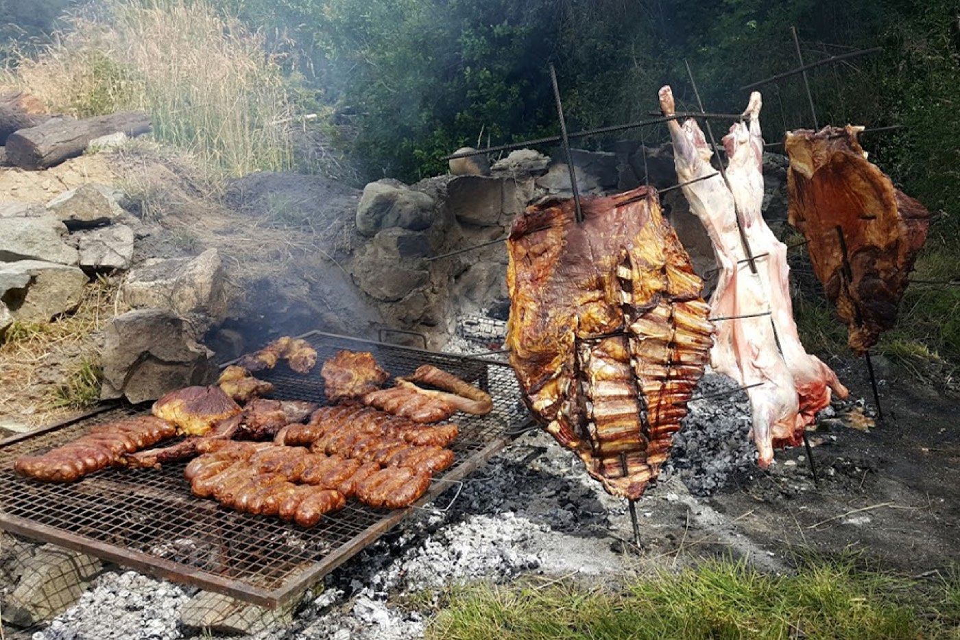 A full asado spread, sausages and ribs on the grill, whole cuts splayed on iron crosses roasting over an open fire