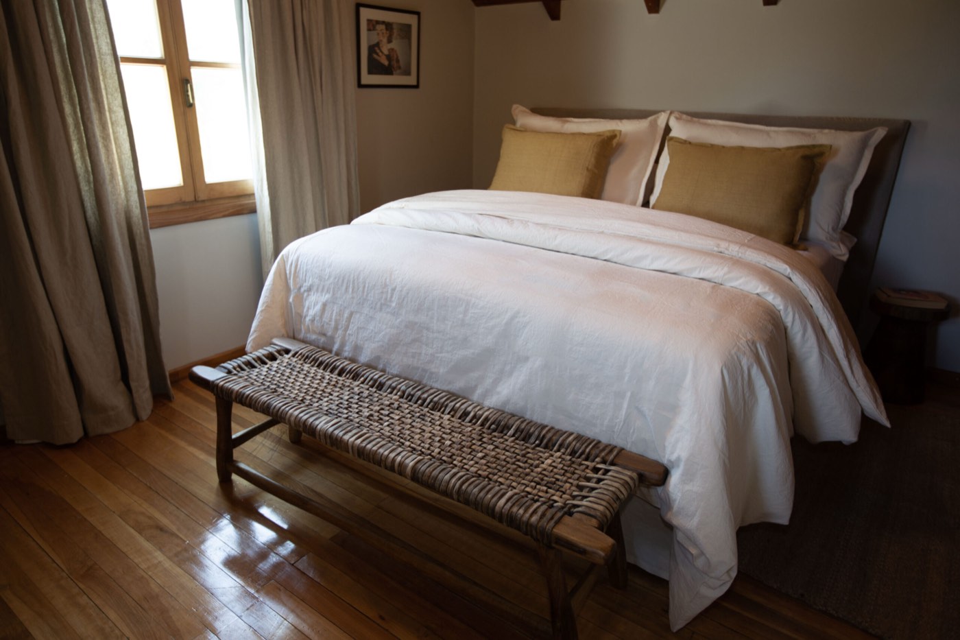 A bedroom with a king bed, olive throw pillows, and a woven bench at its foot