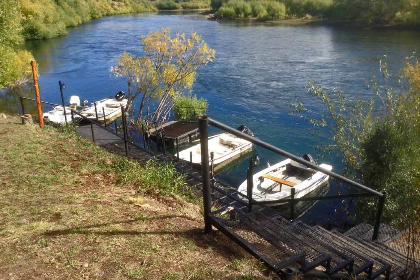 A row of small motorboats moored at a dock, the gangway leading down to a sunlit river