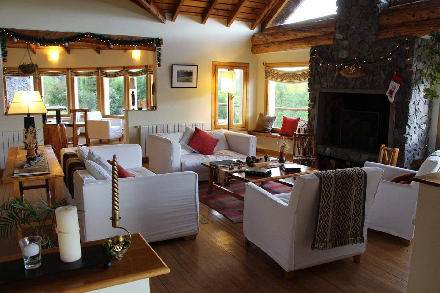 A living room warmed by string lights and holiday décor, white sofas facing a lit stone fireplace with a small wooden fish above the mantle