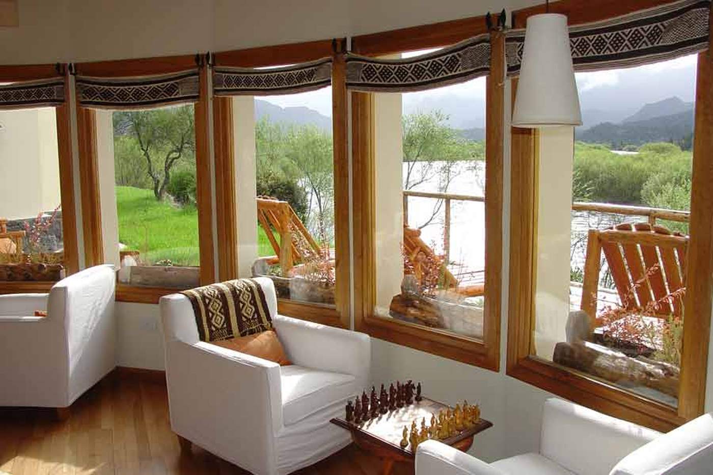 A round sunroom with floor-to-ceiling windows on every side, white armchairs, and a wooden chess set