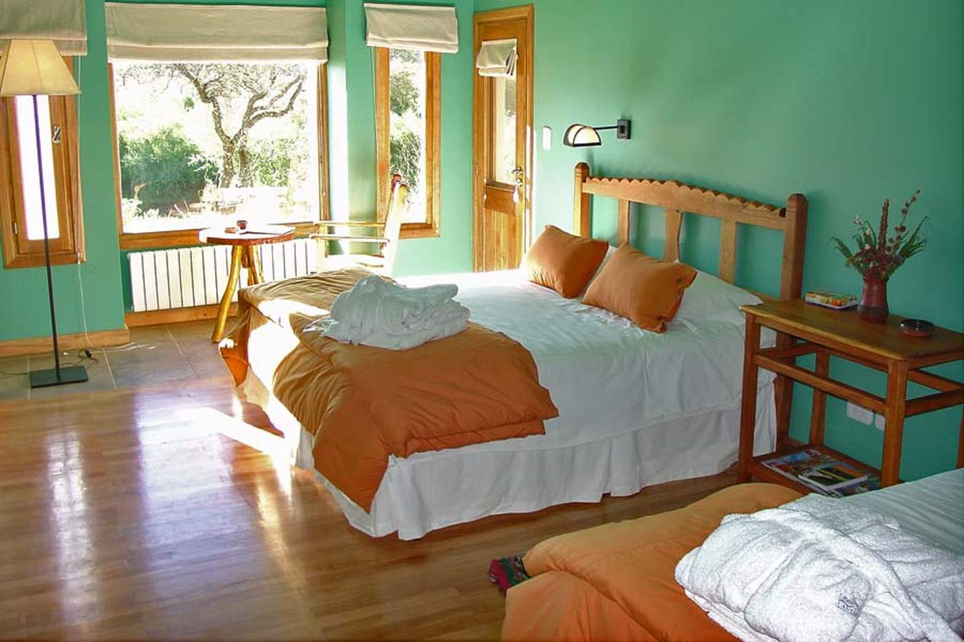 A guest room with orange-and-white bedding, rolled white towels, and a small writing table beside a window