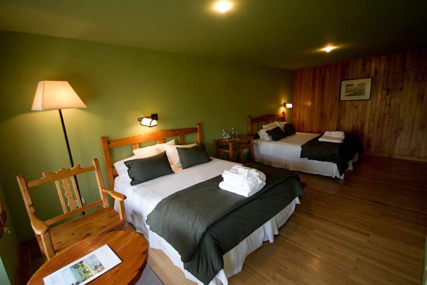 A twin room with a wood-paneled accent wall, olive-green walls, and matching black-and-white bedding on both beds