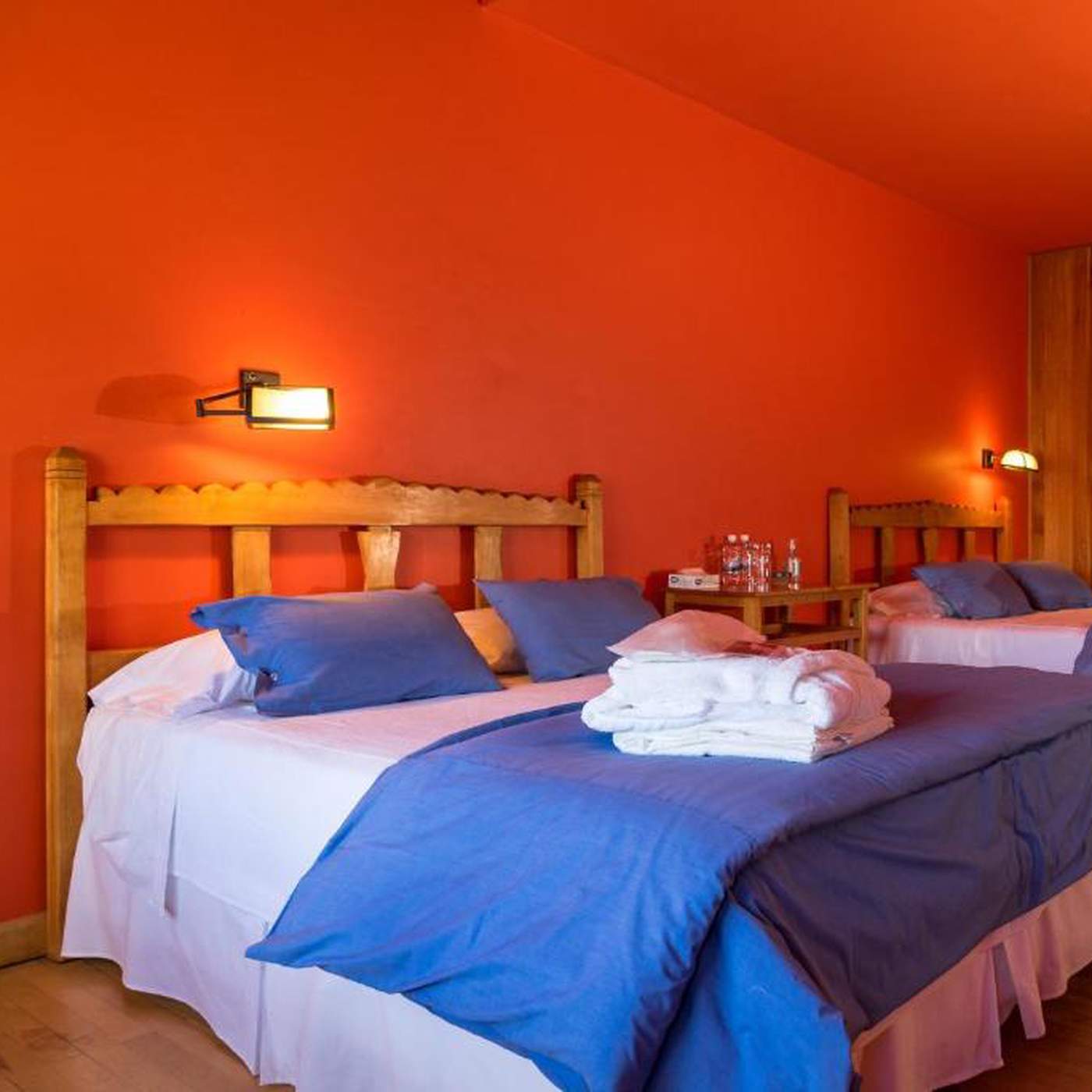 A twin room in bold orange, with blue bed linens and a shared nightstand between the two beds