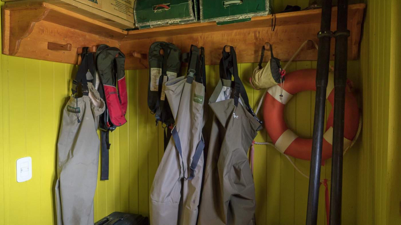 Waders, boots, and life jackets hanging from pegs in the gear room, a life preserver ring on the wall beside them