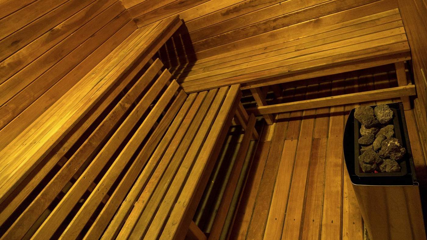 The interior of a wood-paneled sauna, slatted benches surrounding a stone heater