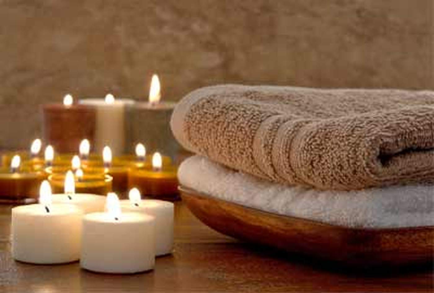 Lit candles beside a stack of folded spa towels on a wooden table