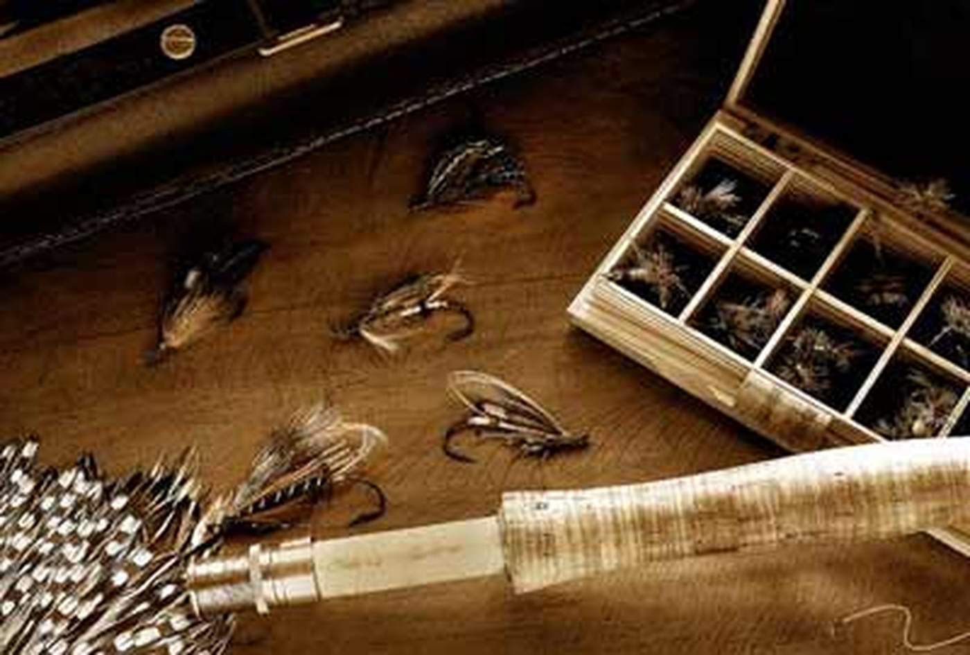 An overhead view of hand-tied flies scattered beside an open fly box and a cork-handled rod