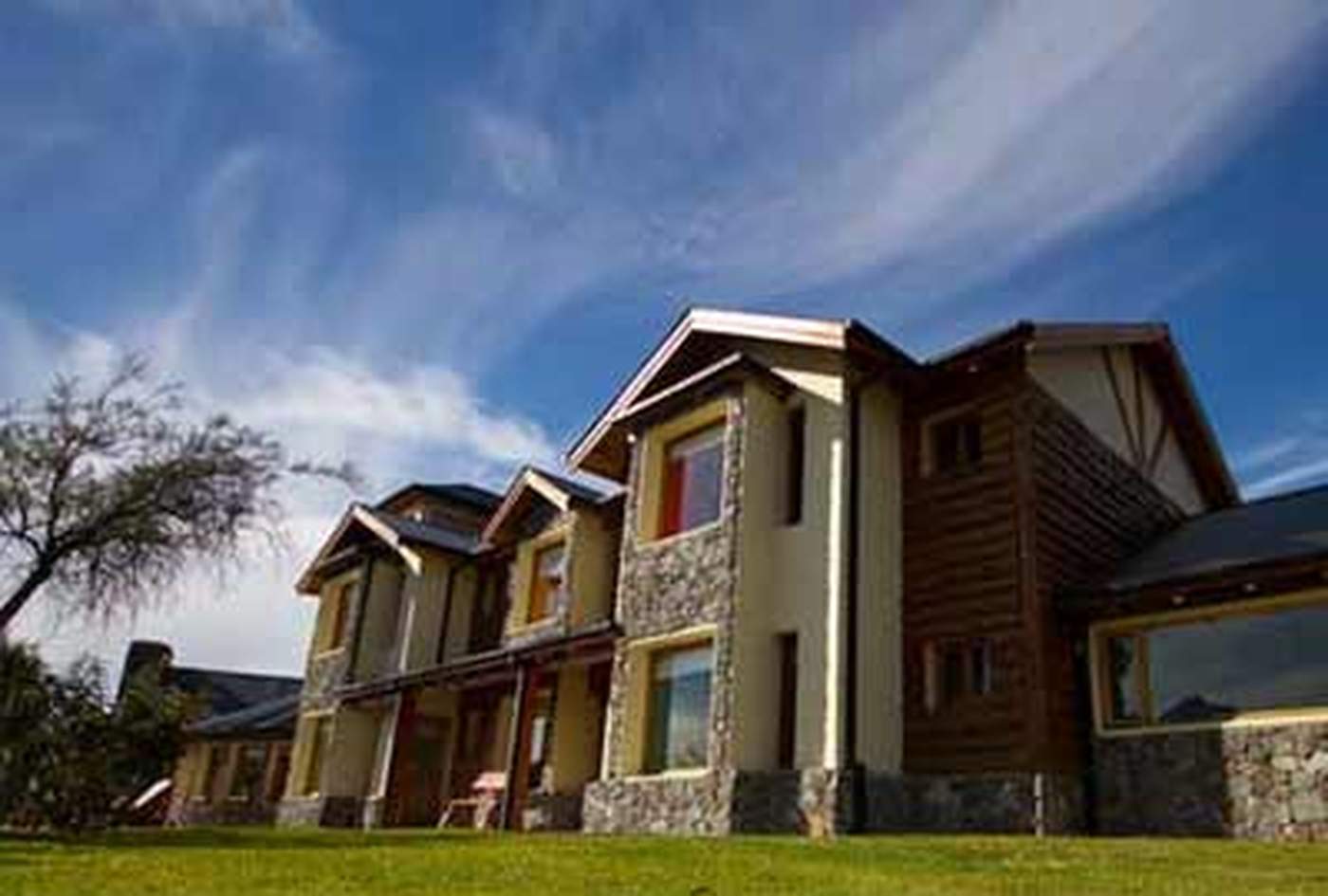 A low-angle view of a stone-and-timber lodge wing against a blue sky