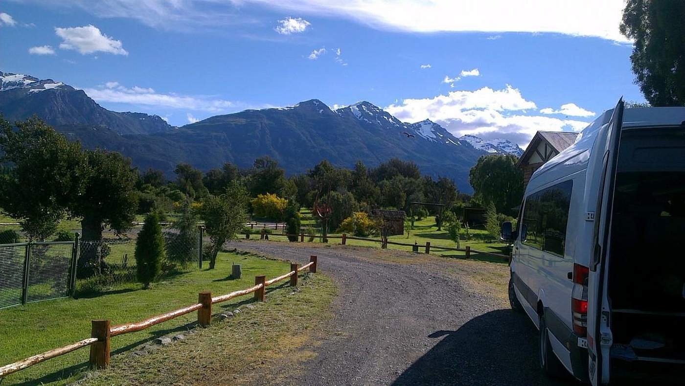 A gravel driveway leading toward the lodge, snow-capped mountains in the distance