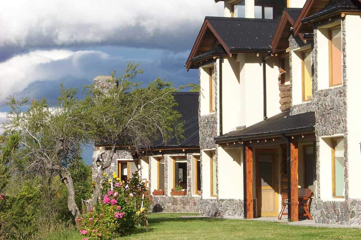 A stone-and-stucco lodge building under a dramatic stormy sky, colorful window glazing and rose bushes below