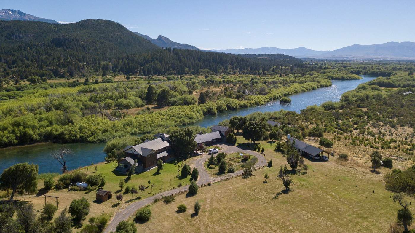 An aerial view of the full lodge complex on a river bend, its buildings and circular driveway surrounded by forest