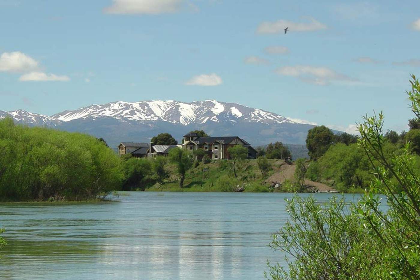A telephoto view across the water toward the lodge complex on the far shore, snow-capped mountains behind