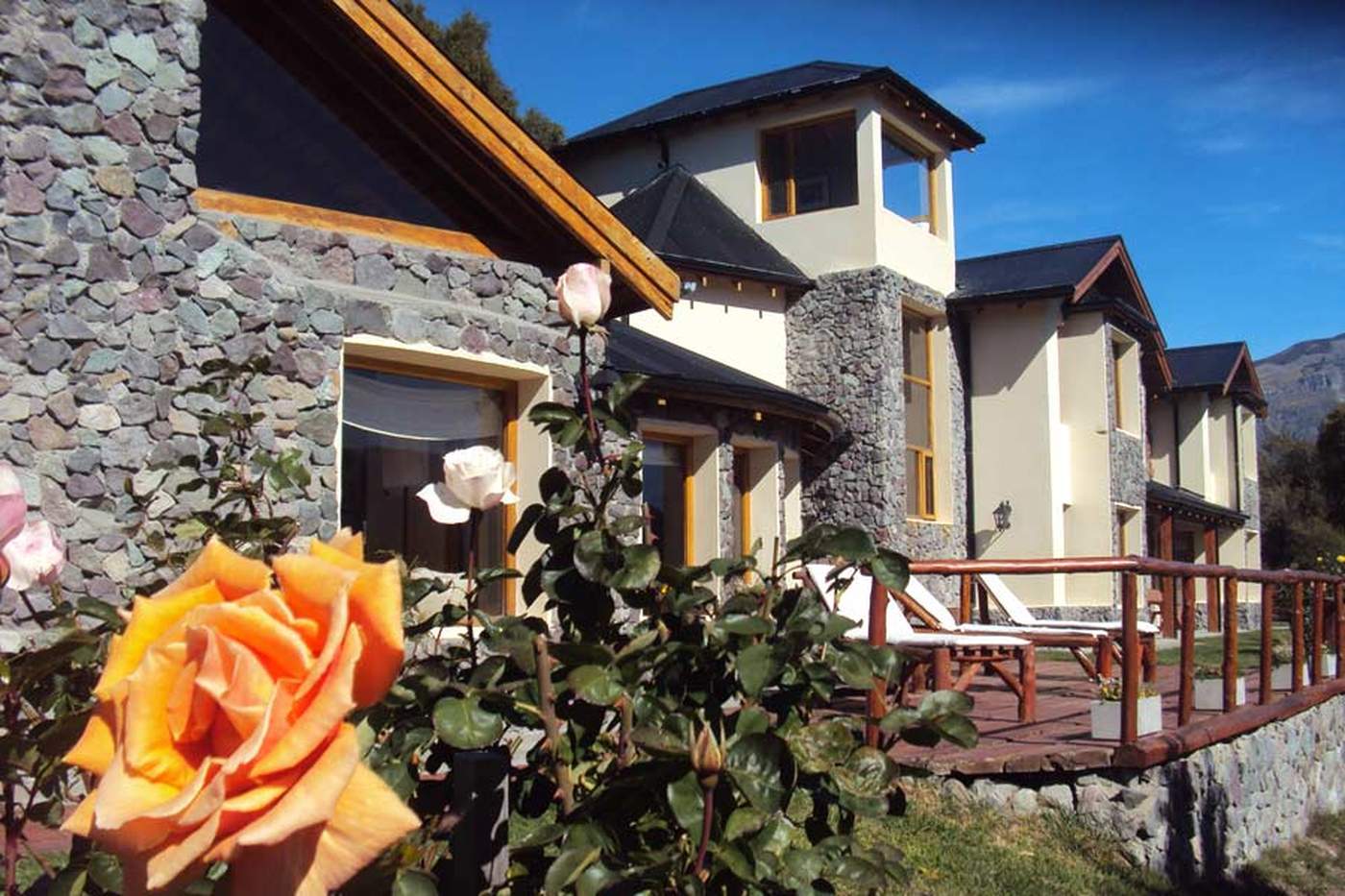 A round, tower-topped lodge wing in stone and stucco, orange and pink roses in the foreground and lounge chairs on the patio