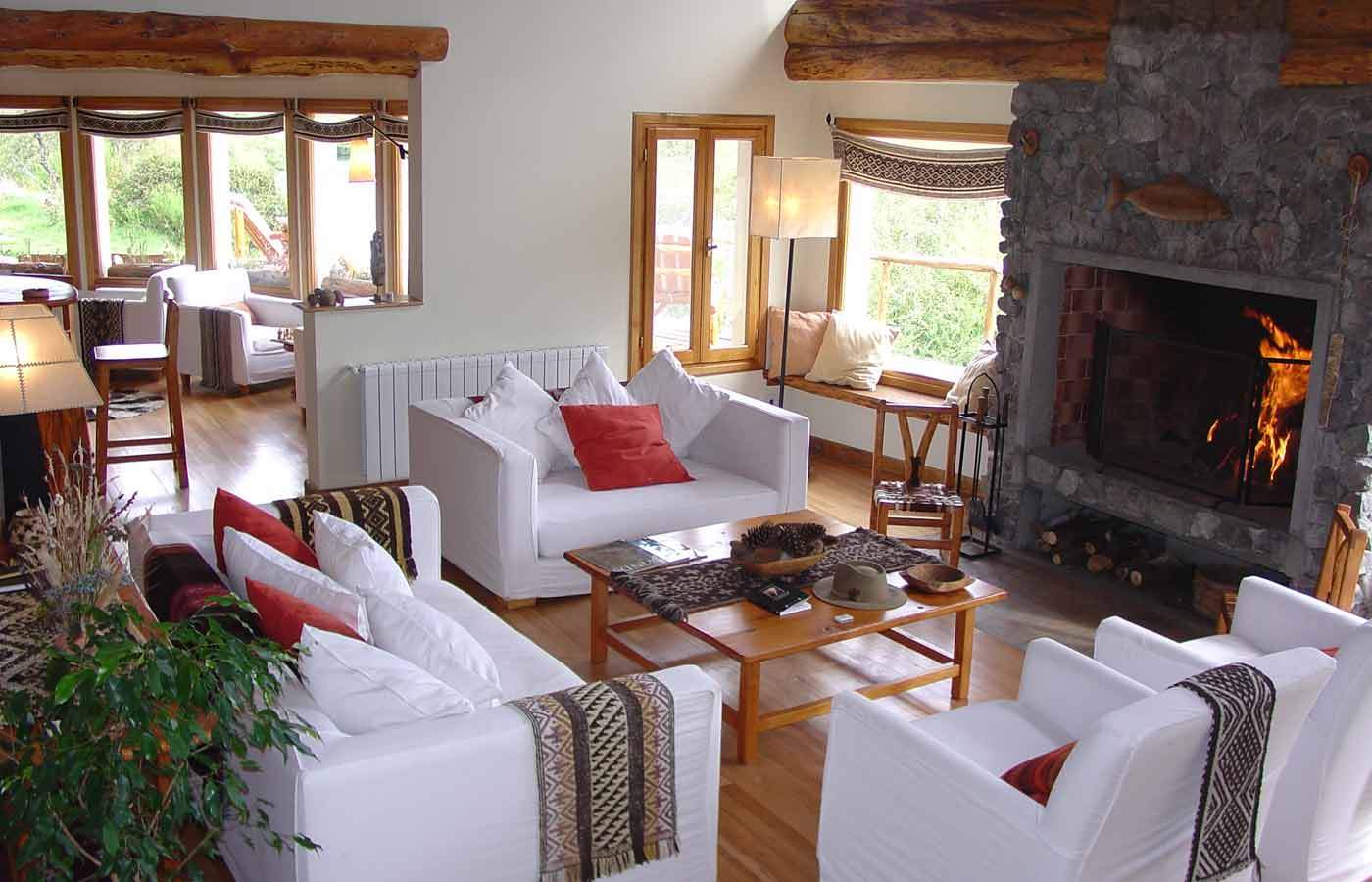 A great room with a crackling stone fireplace, white sofas with patterned throws, and French doors opening onto the deck