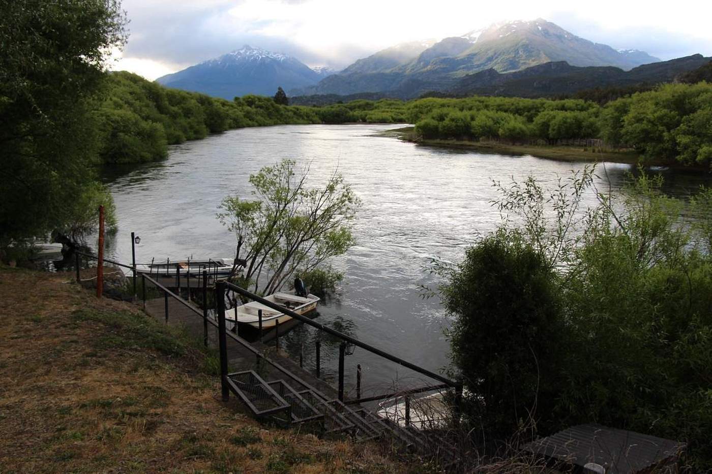 Fishing boats tied up at a dock as evening clouds gather over the mountains, the river bending away downstream