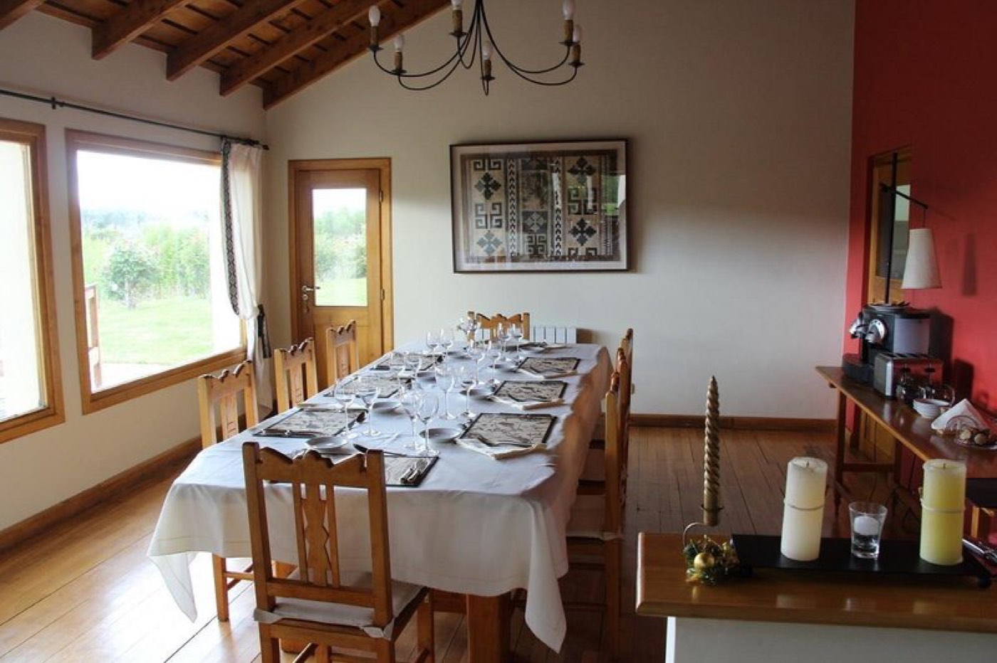 A formal dining room with a long table set for a group beneath a wood-beam ceiling and a woven wall hanging