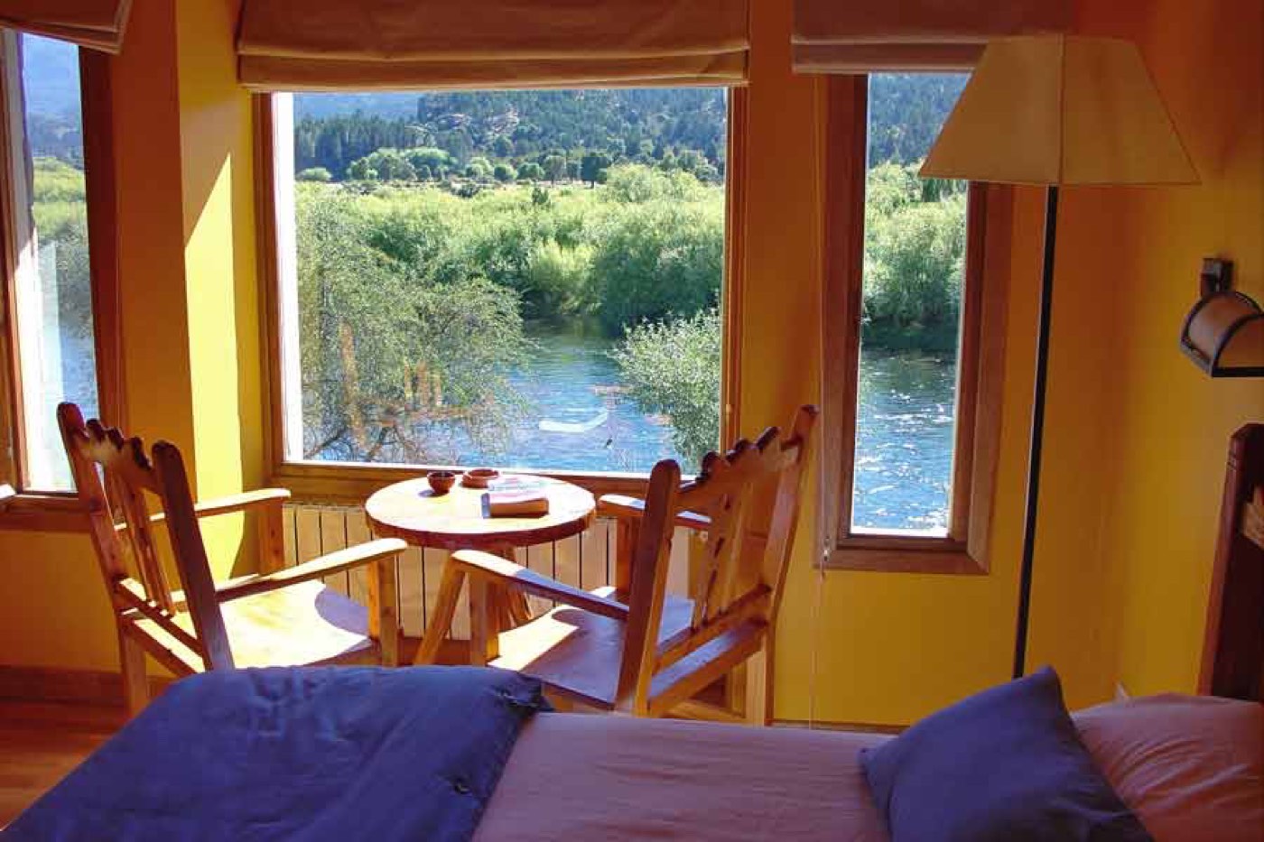 A room overlooking the river through large windows, with a small round table and chairs beside the bed