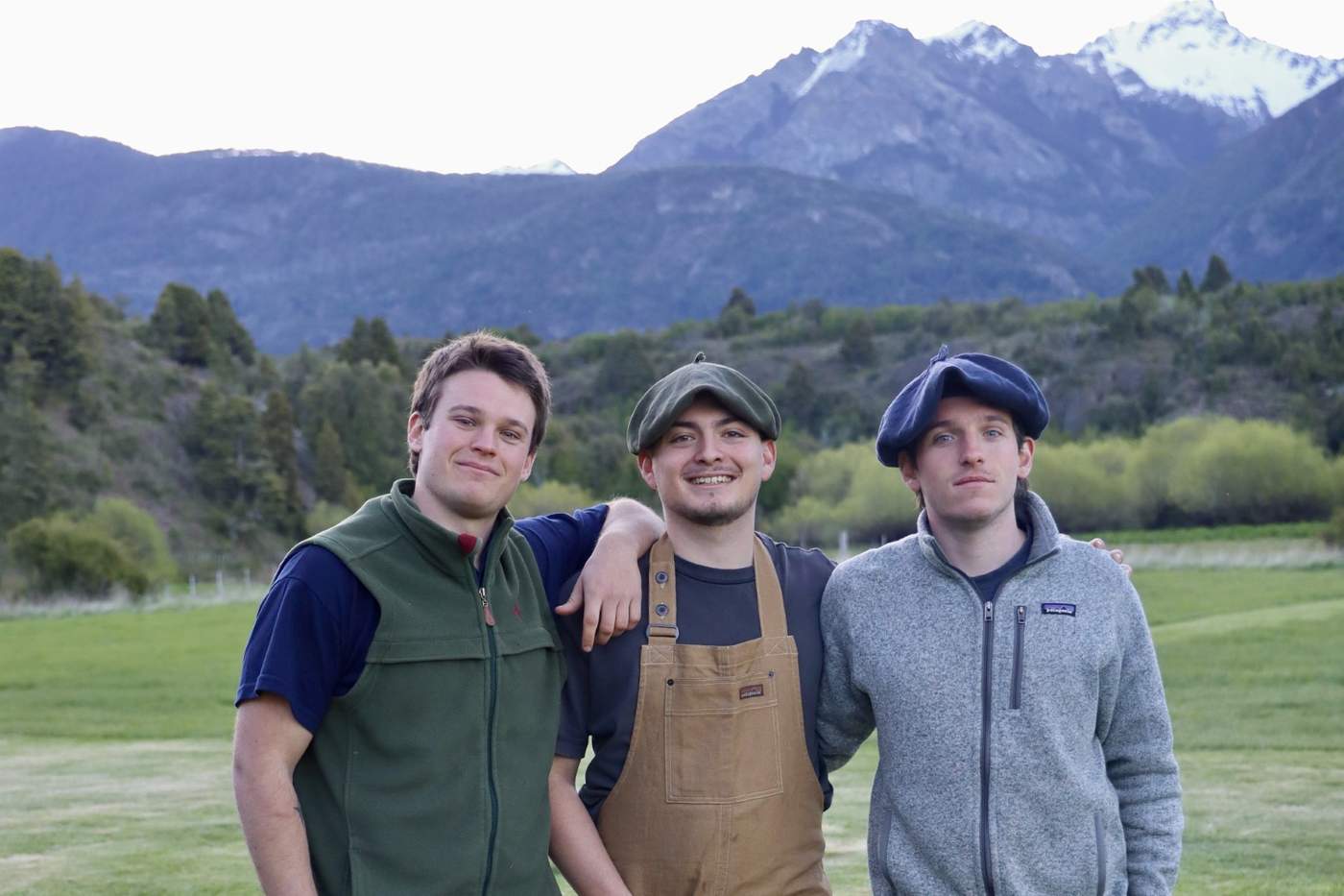 Three of the lodge's hosts posing together on the lawn, mountains rising behind them