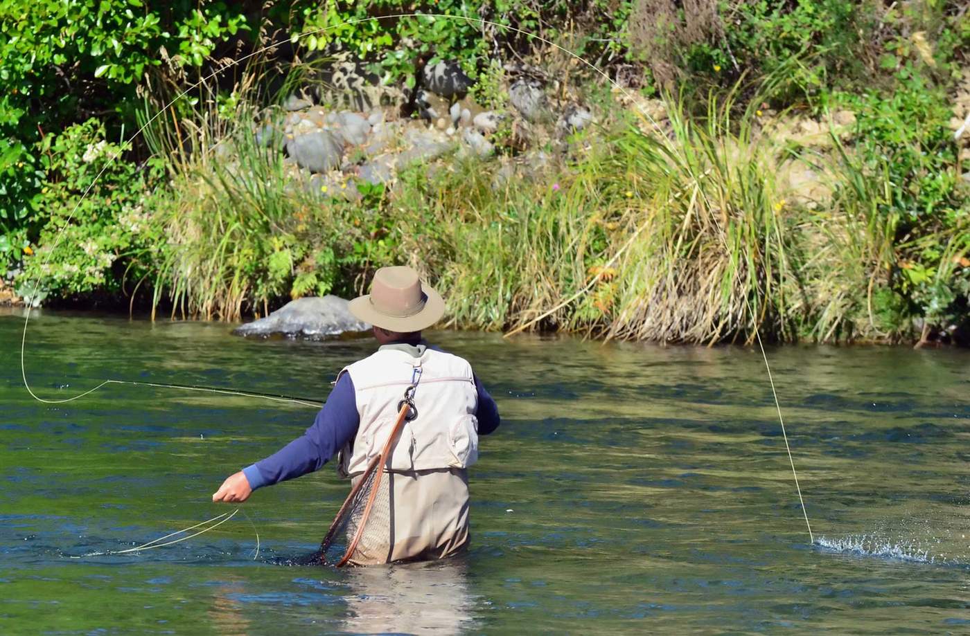 An angler seen from behind, casting a fly line across a wide river