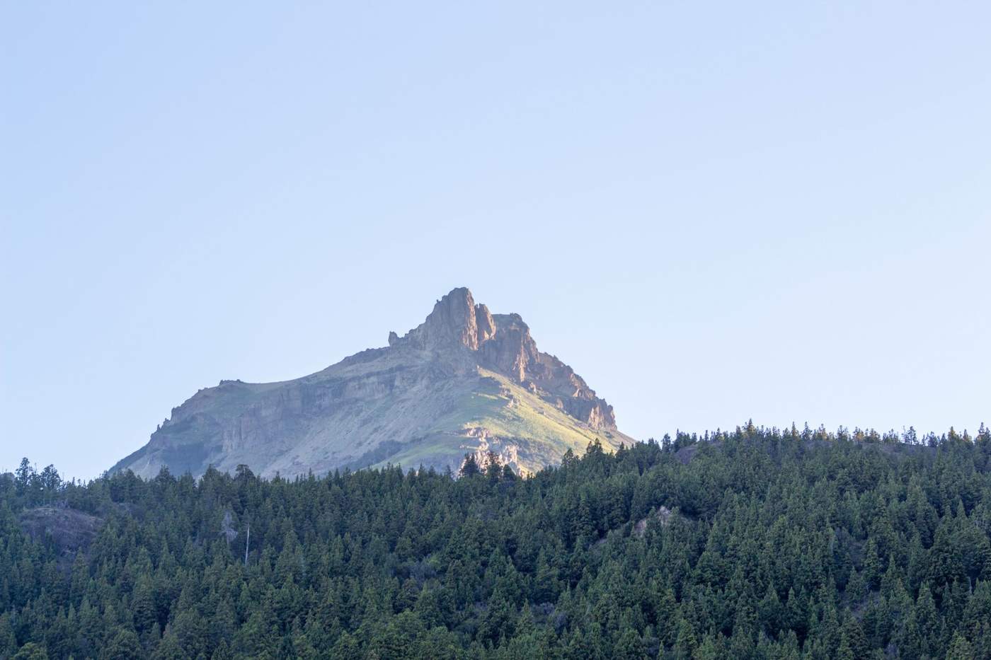 A jagged, sunlit rock peak rising above a ridge of dense forest