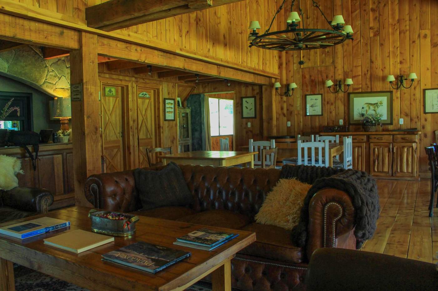The lodge's great room, with leather chesterfield sofas beneath a wagon-wheel chandelier, a dining table and mounted wildlife trophies beyond