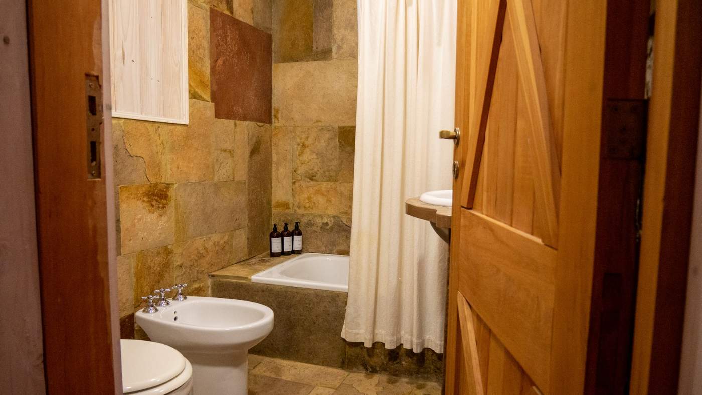 A stone-tiled bathroom with a soaking tub, pedestal sink, and bidet, amenities lined along the counter
