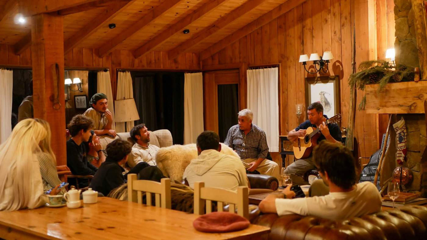 An evening gathering in the great room, guests seated around a guitarist playing by the fire