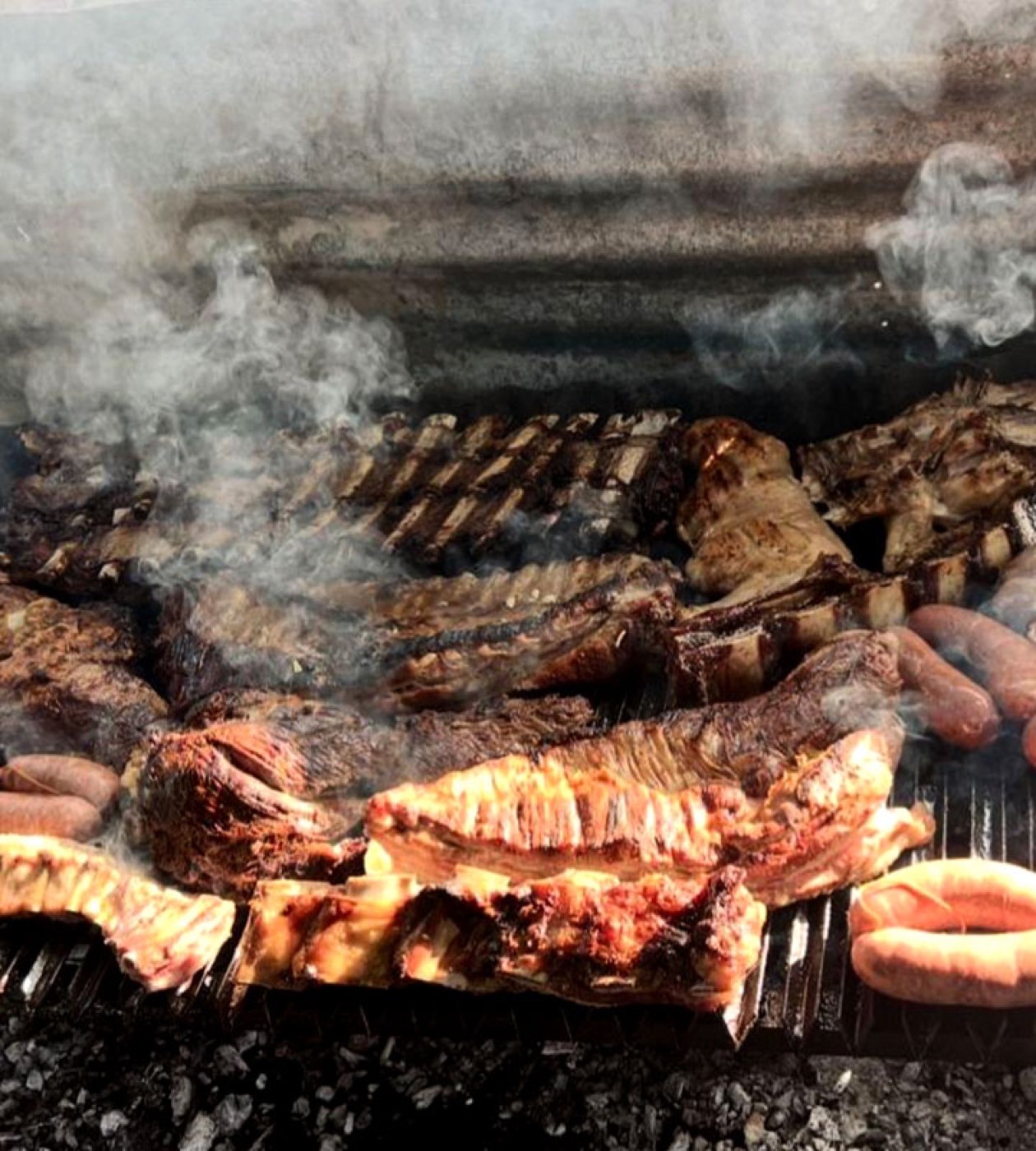 A full asado grill of ribs and sausages smoking over open coals