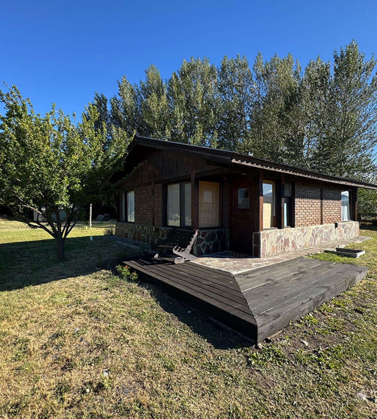 A single-story timber lodge building with a covered deck and a stone foundation