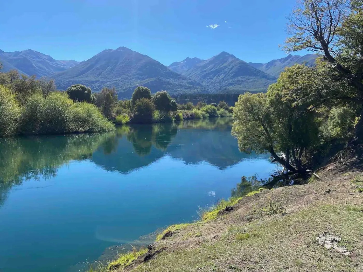 The river bending past a gravel bank, mountains and trees mirrored in the still water